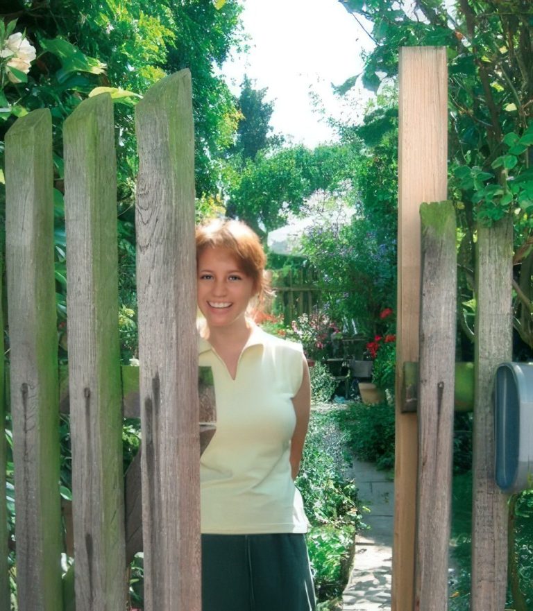 Lächelnde junge Frau Lächelnde junge Frau öffnet Gartentor